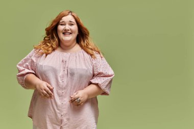 A plus size woman in a pink blouse smiles brightly against a green background. clipart