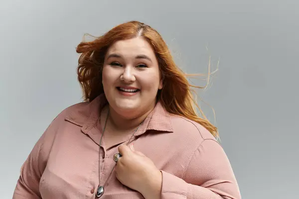 stock image A plus-size woman with red hair smiles confidently, her windblown hair adding movement to the image.