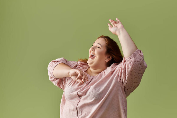 A woman in a pink blouse dances with joy against a green background.