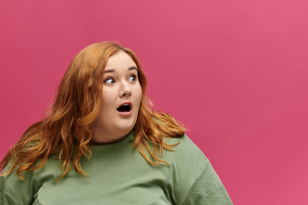 A woman with long red hair and a surprised expression, wearing a green top, looks to the right.