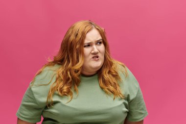 A woman with red hair wearing a green shirt looks away from the camera with a look of frustration. clipart