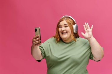 Yeşil tişörtlü bir kadın telefonuyla görüntülü konuşma yaparken gülümsüyor..