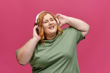 Kızıl saçlı bir kadın, kulaklık ve yeşil tişört giyerken müzik eşliğinde şarkı söylüyor..
