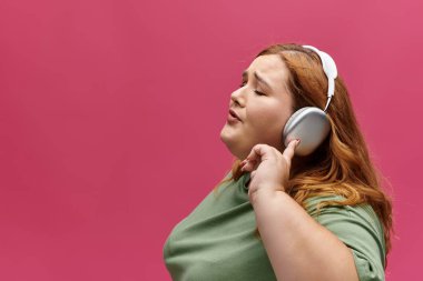 Yeşil tişörtlü bir kadın beyaz kulaklıklarla müzik eşliğinde şarkı söylüyor, gözleri neşe içinde kapalı..