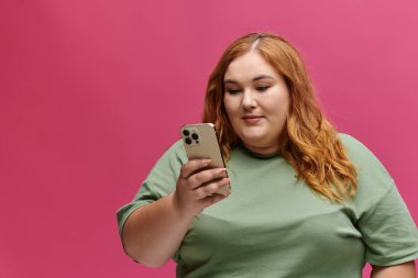 Yeşil tişörtlü bir kadın telefonuna dikkatle bakıyor, ifadesi odaklanmış..
