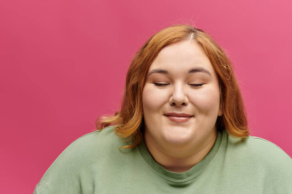 На розовом фоне женщина плюсового роста трезво улыбается, глаза закрыты.