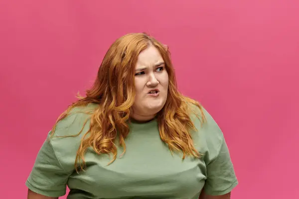 stock image A woman with red hair wearing a green shirt looks away from the camera with a look of frustration.