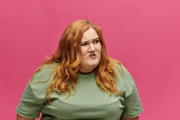 A woman with red hair wearing a green shirt looks away from the camera with a look of frustration.