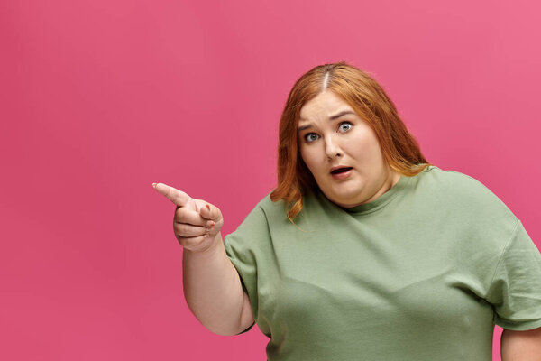 A woman in a green shirt points to the side, her face expressing shock and disbelief.