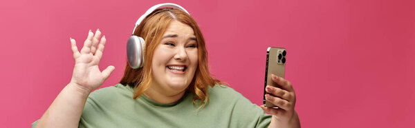 Женщина с длинными рыжими волосами, улыбаясь и глядя на телефон.