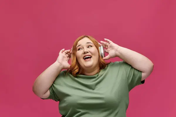 stock image A plus size woman in a green shirt listens to music while smiling and looking up.