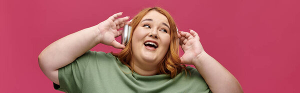 Женщина с рыжими волосами и зеленой рубашкой поет под музыку в наушниках.