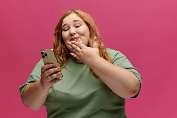 Женщина широко улыбается, глядя на свой телефон, ее рука с удивлением закрывает рот..