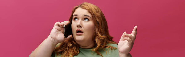 Женщина с длинными рыжими волосами говорит по телефону, глядя вверх с удивленным выражением лица.