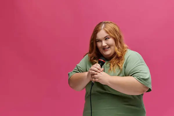 stock image A woman smiles while holding a microphone in front of a pink background.