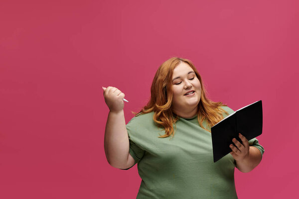 Женщина в зеленой рубашке читает книгу, держа ручку в другой руке, улыбаясь..