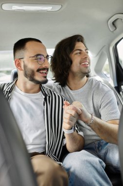 Arabadayken iki adam el ele tutuşup gülümsüyor..