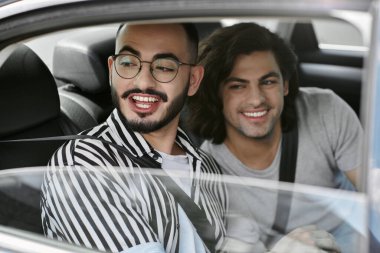 Mutlu ve tasasız görünen iki adam, bir arabanın arka koltuğunda yan yana otururlar..