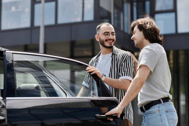 Two men stand beside a car, smiling and laughing together. clipart