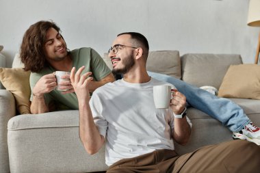 İki adam kanepede rahatlar, gülümser ve kahvelerinin tadını çıkarırlar..