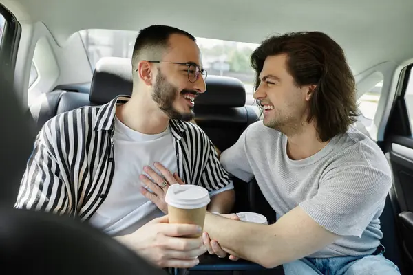 stock image A gay couple laughs together in the backseat of a car, enjoying coffee.