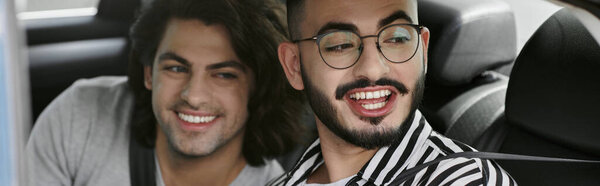 Двое мужчин сидят на заднем сиденье машины, улыбаются и смеются вместе.