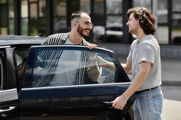 stock image Two men smile at each other, one opening a car door.