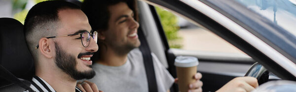 A gay couple smiles and laughs as they enjoy a sunny car ride.