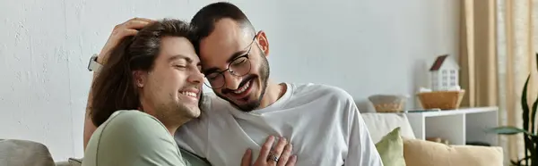 stock image Two men embrace on a couch, smiling and laughing together.