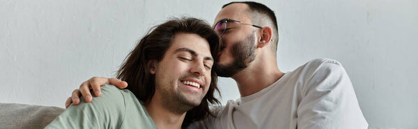 На диване сидит гей-пара, один мужчина любовно целует другого на полу..