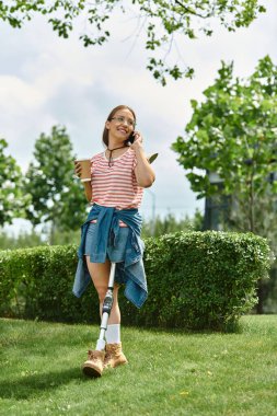 A young woman in a casual summer outfit walks through a park, smiling as she talks on her phone and enjoys a refreshing beverage. clipart