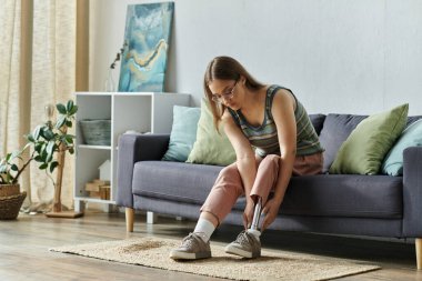 Oturma odasındaki kanepede oturan genç bir kadın giydiği protez bacağı düzeltiyor..