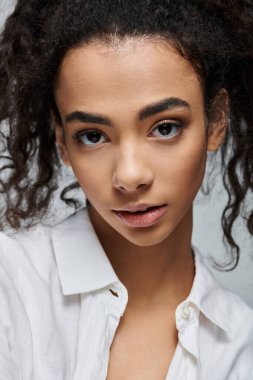 Beyaz gömlekli kıvırcık siyah saçlı genç bir kadın kameraya bakıyor..