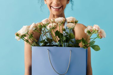 A beautiful young woman in a dress smiles radiantly, holding a bag full of flowers against a bright blue backdrop. clipart