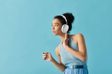 Mavi elbiseli ve kulaklıklı genç bir kadın mavi arka planda müzik dinlemekten hoşlanır..