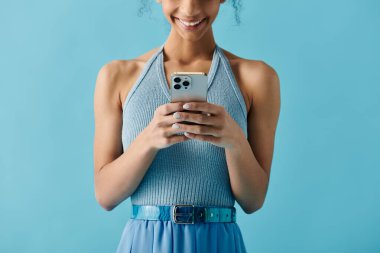 Mavi elbiseli genç bir kadın telefonunu kullanırken gülümsüyor, canlı ve neşeli bir ifade sergiliyor..