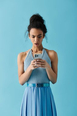 A young woman in a blue dress looks shocked as she reads a message on her phone. clipart