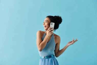 A young African American woman in a blue dress smiles brightly while talking on her phone against a light blue background. clipart