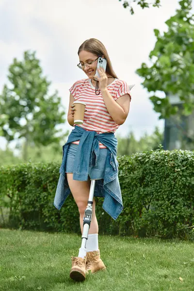 stock image A young woman with a prosthetic leg smiles while talking on the phone and enjoying a coffee in a park setting.