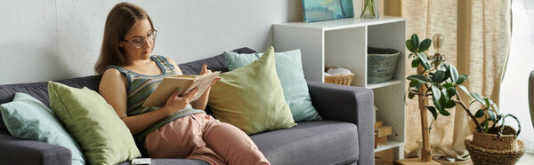 A young woman with a prosthetic leg relaxes on a sofa in her living room, reading a book.