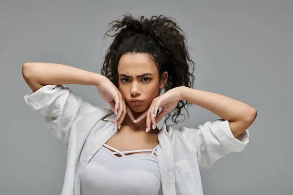 stock image A young African American woman with curly hair poses in a white shirt against a gray backdrop.