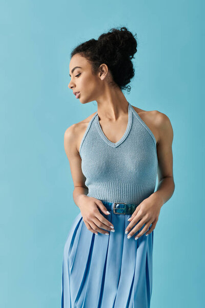 Молодая женщина в узком топе и юбке, ее волосы оттянуты назад в булочке, позирует на фоне голубого неба.