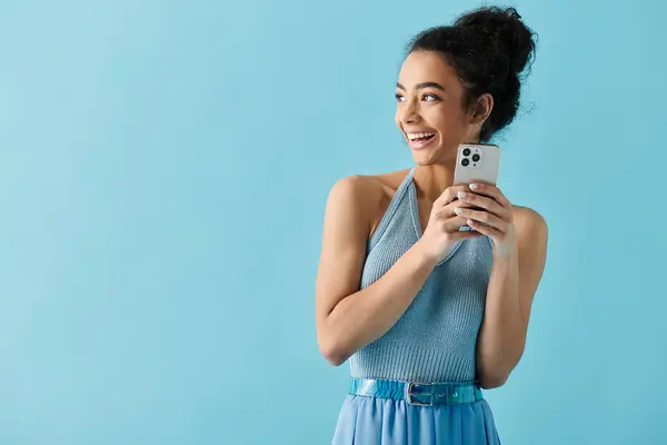 stock image A young woman with a bright smile, dressed in a blue outfit, looks to her right while holding her phone.