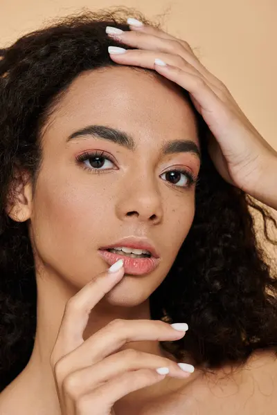 Stock image A young woman with curly hair gazes into the camera, her hand gently touching her lips.