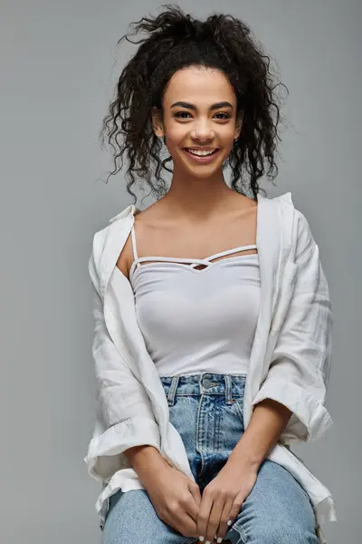 stock image A young African American woman with curly hair smiles brightly as she poses against a grey backdrop.