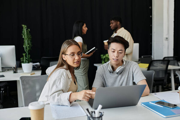 Two young colleagues work together on a laptop, discussing ideas for their new venture.