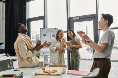 Dört meslektaş, modern bir ofiste pizza molası veriyor..