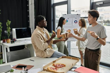 Dört genç iş arkadaşı, modern bir ofiste pizza ve kahvenin tadını çıkarırken işe ara veriyor..