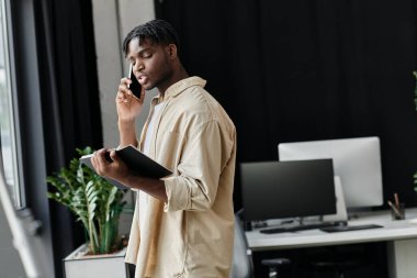 Genç bir adam, muhtemelen yeni başlayan bir kurucu, elinde bir defterle telefonda yürüyor..