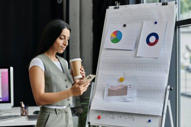 A woman in a modern office setting, holding a coffee cup, and reviewing data on her phone. clipart